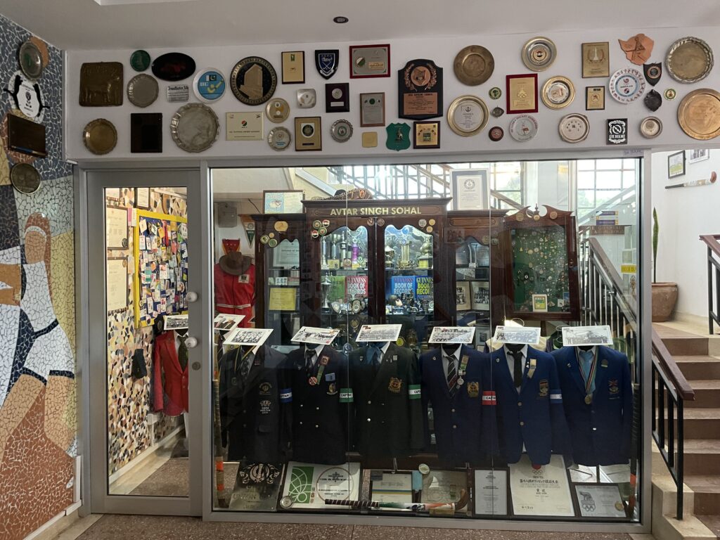 A glass wall separates the viewer from a room full of memorabilia: cabinets of medals and trophies and a long row of mannequins adorned with hockey blazers.