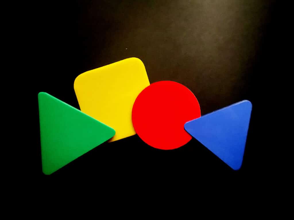 An unusual set of hockey umpires' warning cards. A green triangle, a yellow square, a red circle, and a blue triangle laid out in a row over a black background.