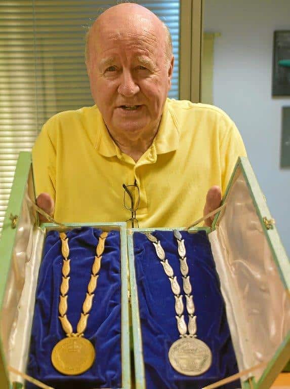 A man, David Jones, wearing a yellow polo shirt showing two athletics medals to camera.