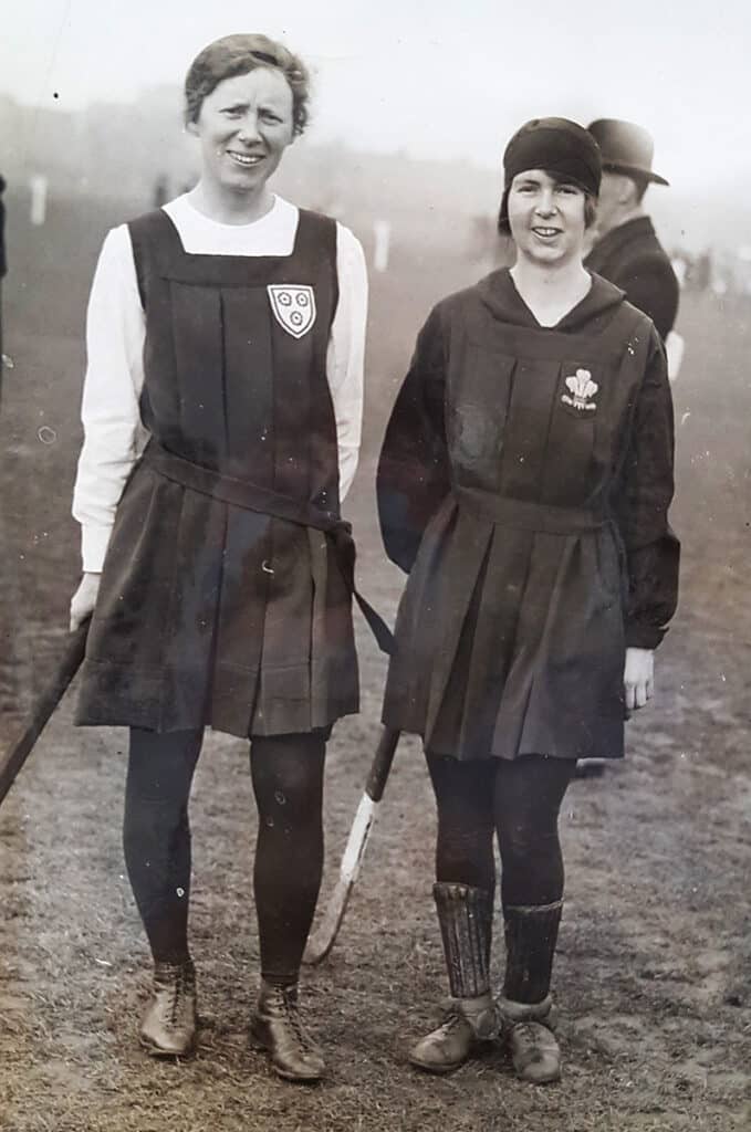 A black and white image of two women in hockey kit, after a match