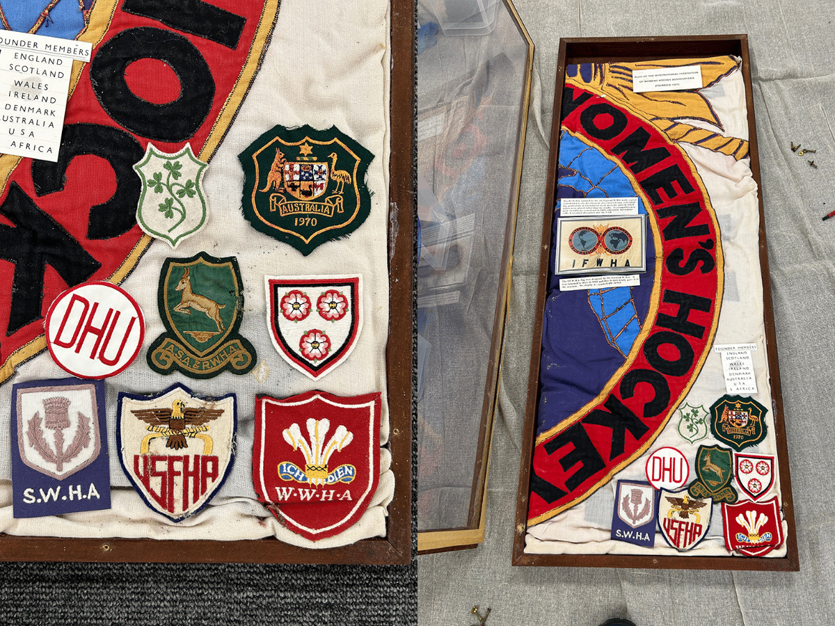 A flag in an original display case with cloth badges representing the founding nations of the IFWHA