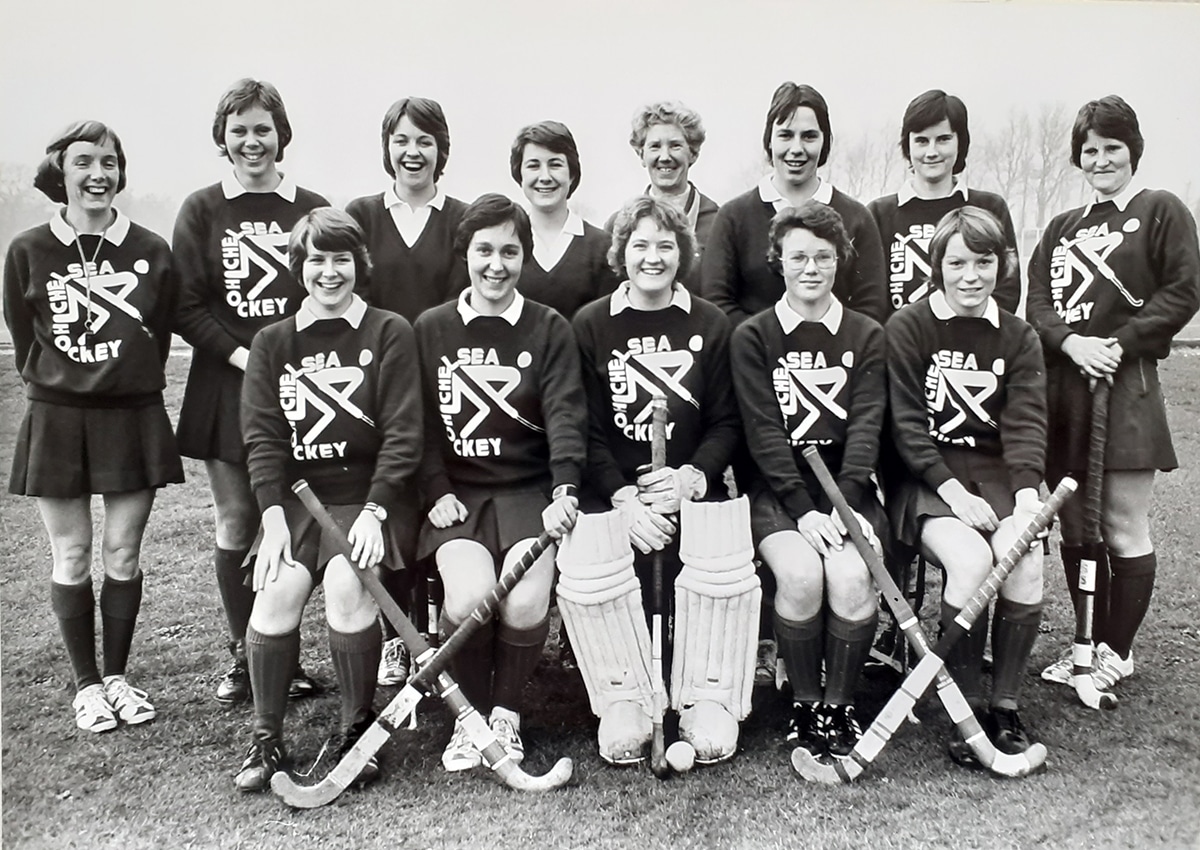 A black and white image of the Chelsea College of Physical Education First XI 1976-77. Chelsea coach and former IFWHA world champion with England, Biddy Burgum is in the back row, fourth from the right.