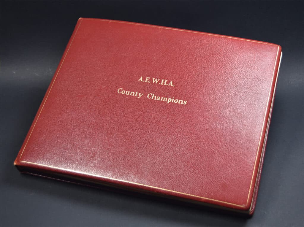 A red leather bound book with gold embossing titled County Championship