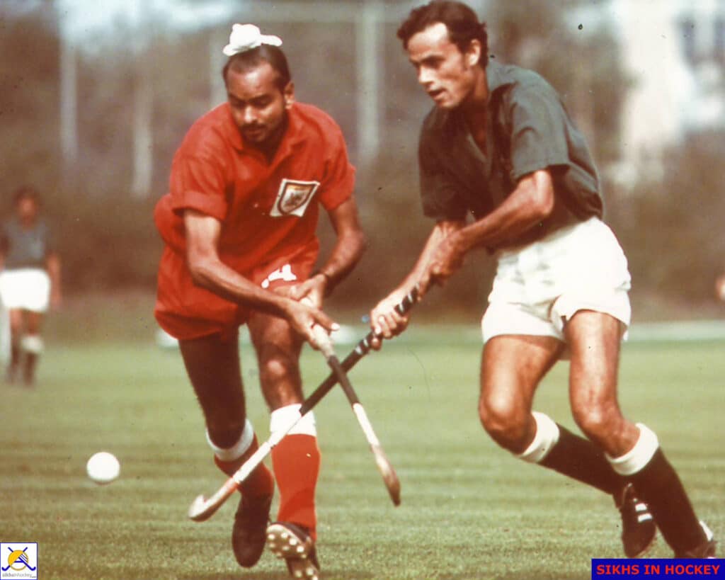 A colour image of two men playing hockey, on opposing teams, challenging for the ball