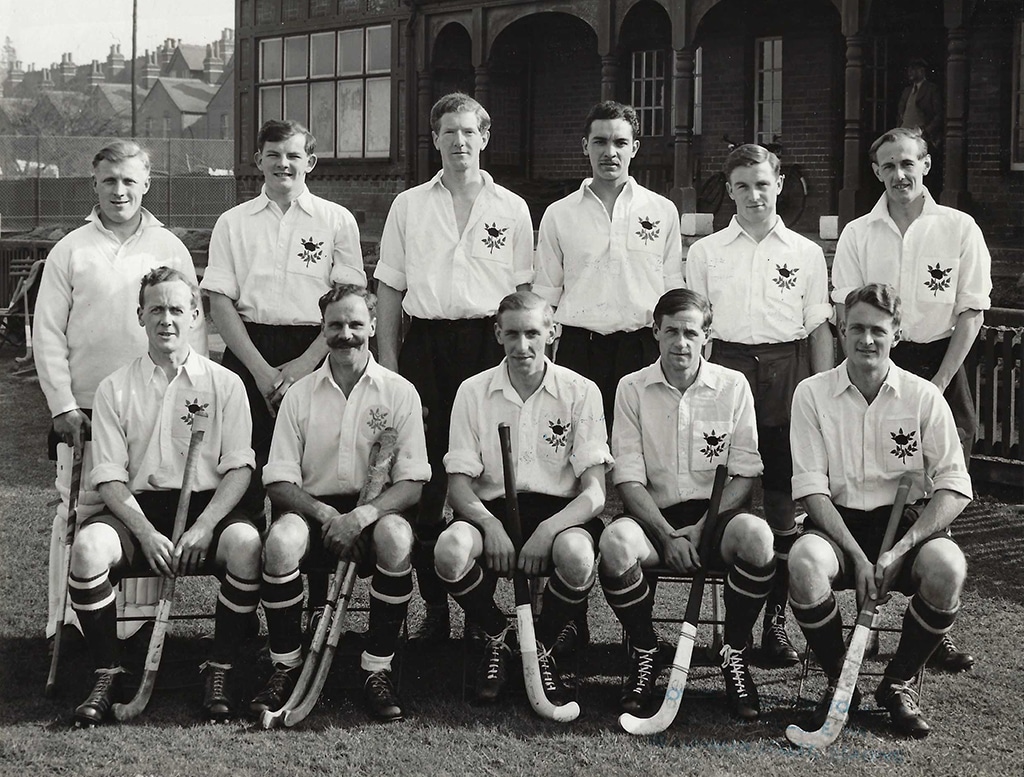 A black and white image of a men's hockey team posing for a photo. They are wearing white button-up shirts with a rose on the breast pocket.