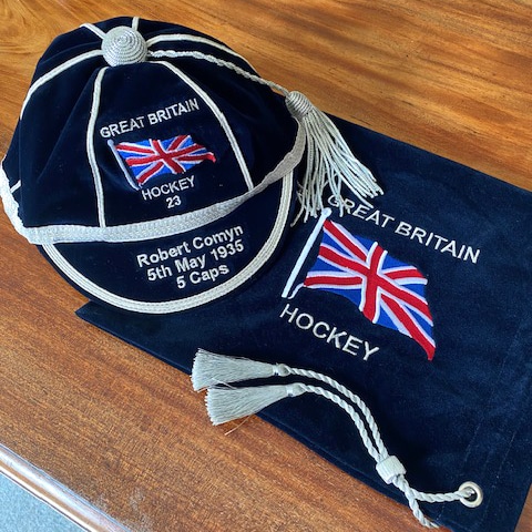 Aerial view of a navy blue cap with silver trim and the Union Flag of Great Britain. Under the cap is a navy blue felt bag with silver tassel and the same logo.