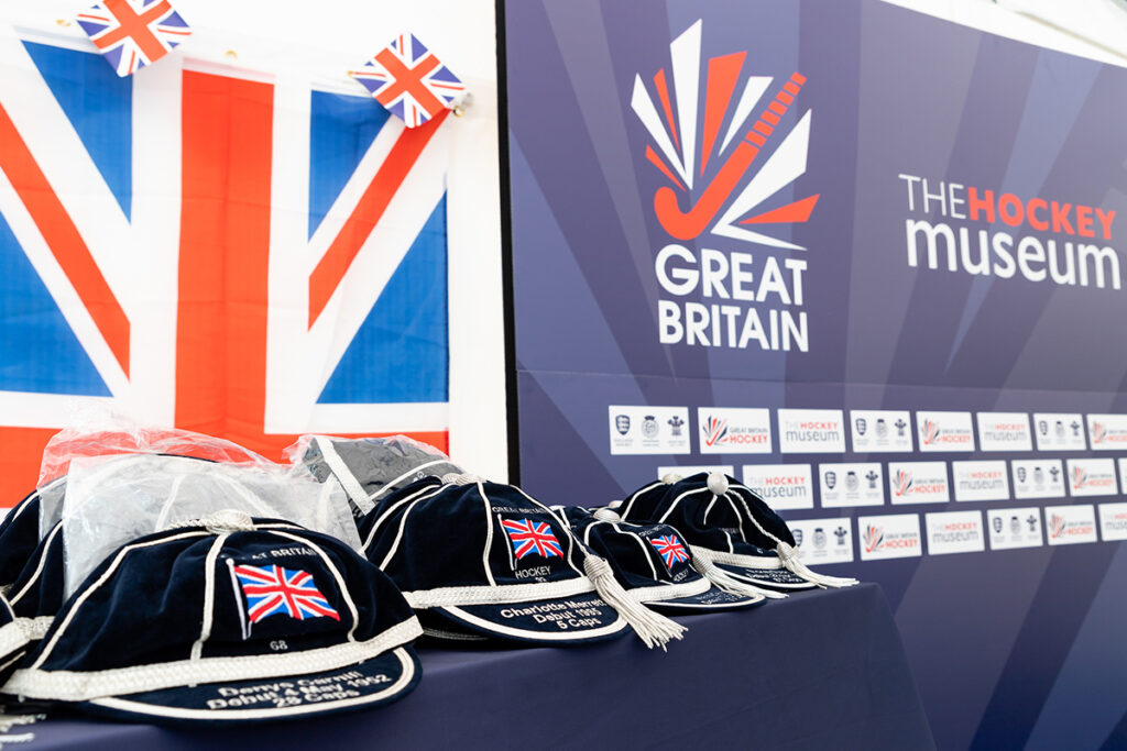Navy honours caps with silver trim and tassels lined up on a table before a presentation event. A large union flag hangs behind.