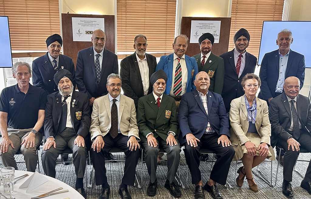 A group of men and one woman posing for a group photo in two rows. The front row is seated, wearing formal attire with some sporting medals and blazers, while the back row stands in suits and turbans.