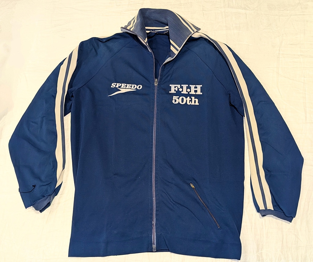 Retro navy blue tracksuit jacket with "Speedo" and "FIH 50th" logos, white stripes. Evokes a feeling of nostalgia.