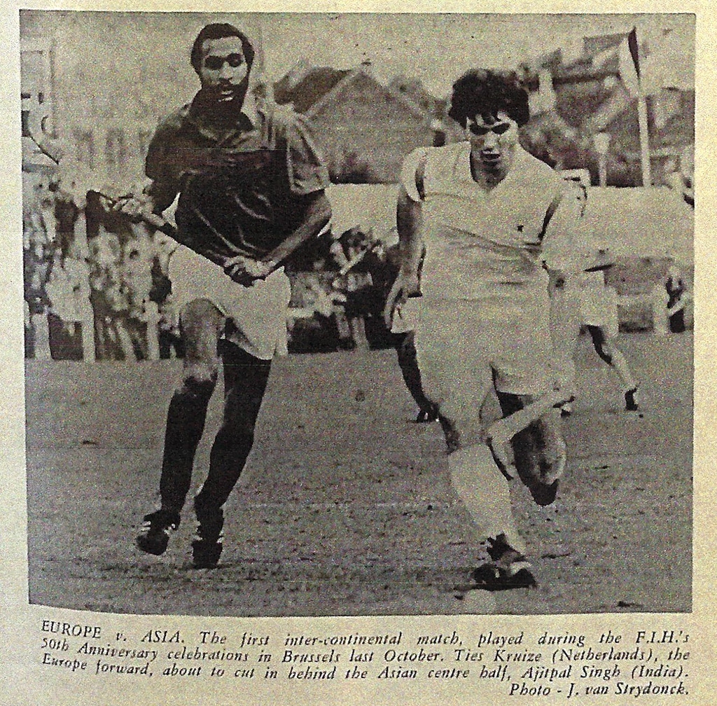 Newspaper cutting showing two male hockey players in action, one European, one Asian. Crowded background. Evokes excitement and competition.