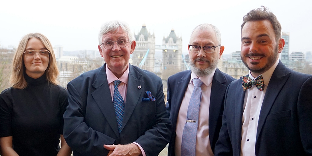 Curatorial Team in 2025 Four smiling, smartly dressed people before a panoramic view of the City of London.