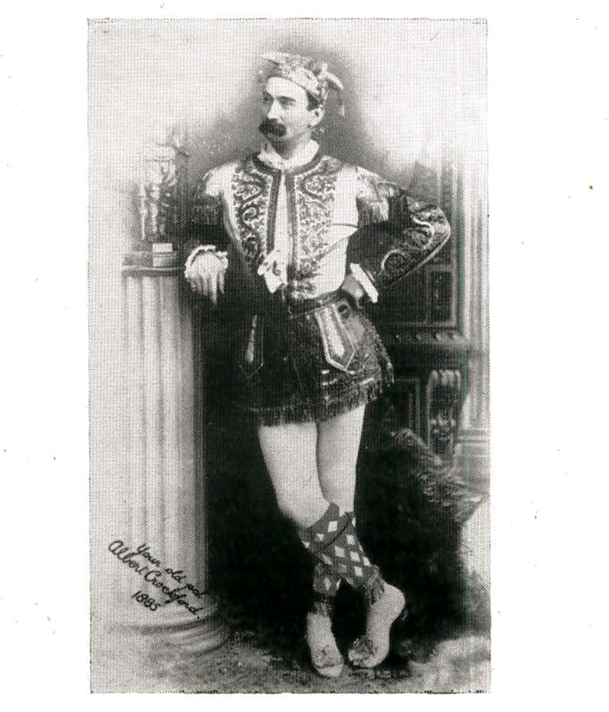 Photograph of a man with a bushy moustache wearing a jester's outfit and long diamond socks.