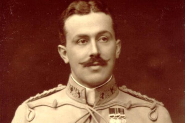 A middle-aged Caucasian man with short dark hair and a thick, pointed moustache. He has no beard and wears an Officer's uniform with medals.