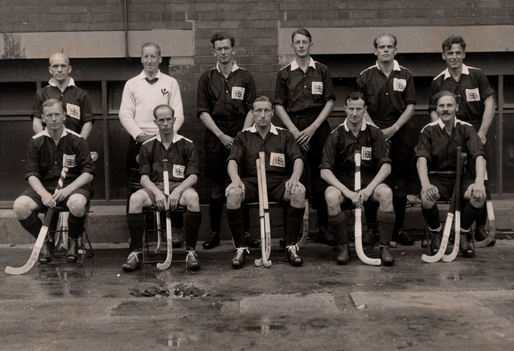 A black and white team photograph of male hockey players in two rows holding hockey sticks.