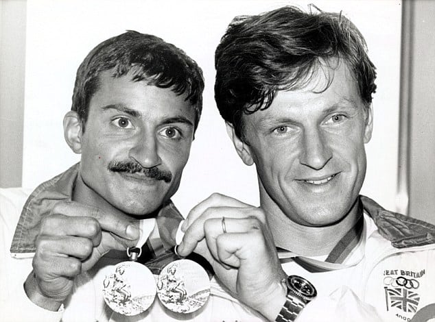 Two young men, one of Asian-heritage and one Caucasian, hold up their Olympic gold medals.
