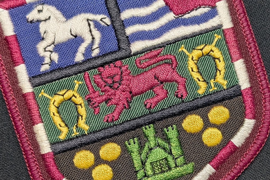 Close-up detail of multi-coloured cloth badge. The iconography includes a horse, a lion holding a sword and a castle.