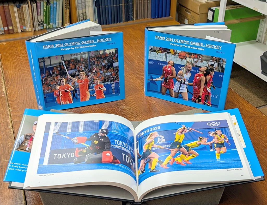 Three large books of photographs on a desk, one of which lies open in the foreground.
