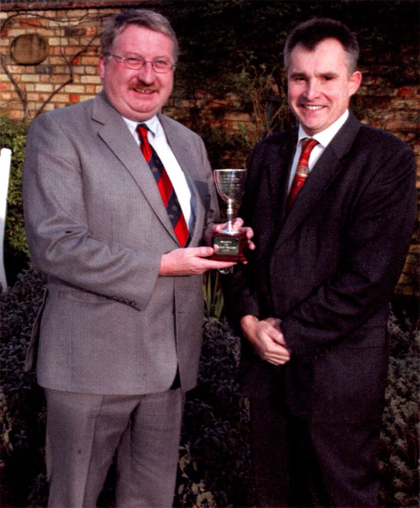 Two men in suits hold a small trophy