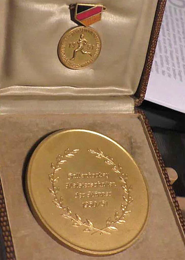 A golden medal sits in a padded case lined with beige-coloured material.