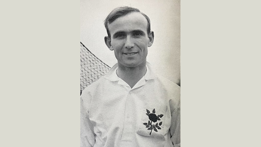 A middle-aged man wearing a white shirt with a rose on the chest.