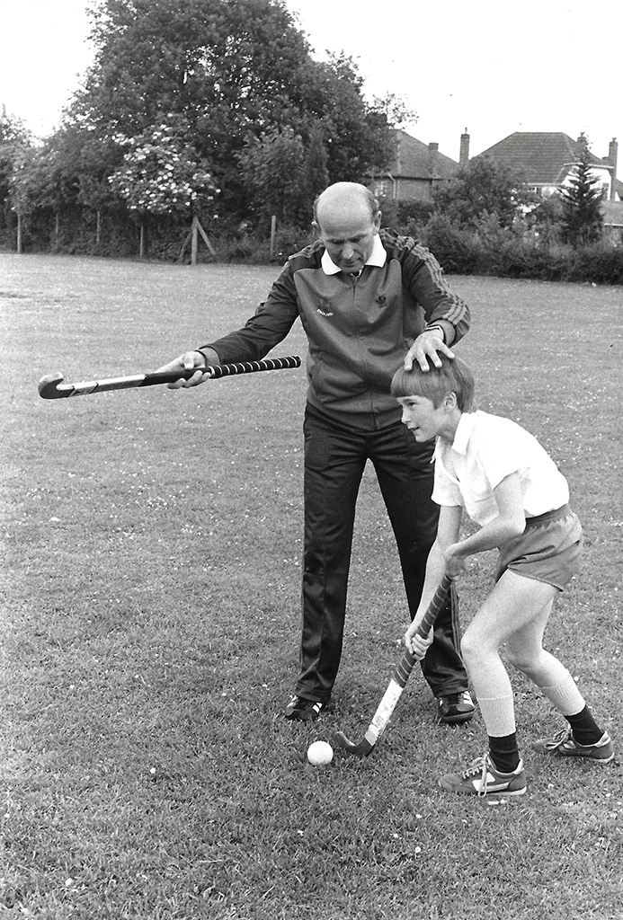 A middle-aged man teaches hockey by placing his hand on the boy's head to encourage correct posture and vision