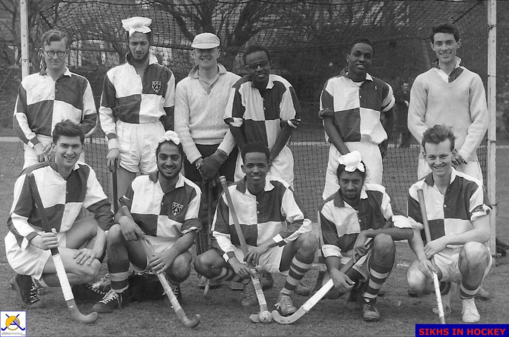 A team of smiling, young male hockey players of various ethnicities stand or crouch in front of a goal.