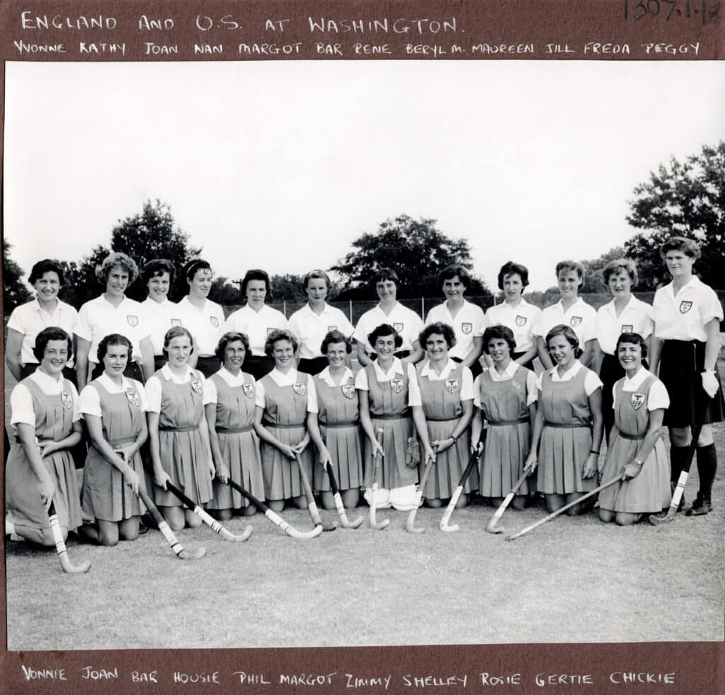 Black and a white photograph of two women's hockey teams in two rows: the back row is standing and the players in the front row, all wearing matching tunics, are kneeling.