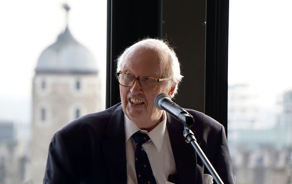 An elderly man in a suit and tie behind a microphone.
