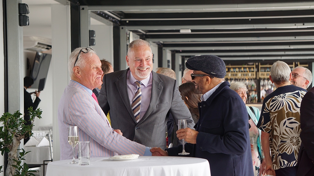 Three smiling men greet each other.