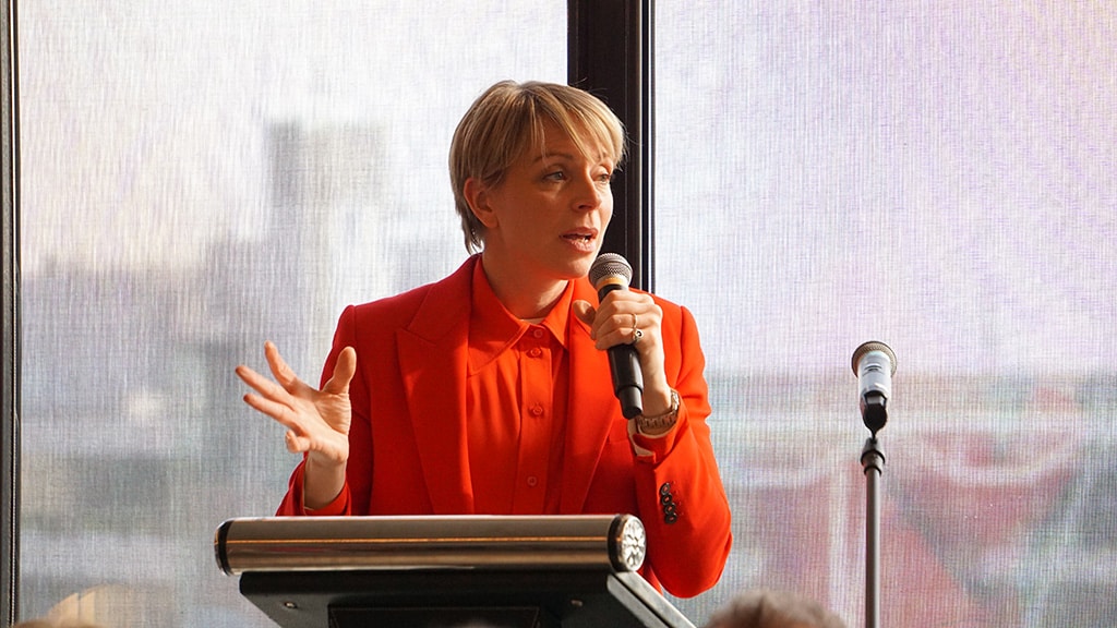 A woman in a red shirt and red blazer gives a speech.