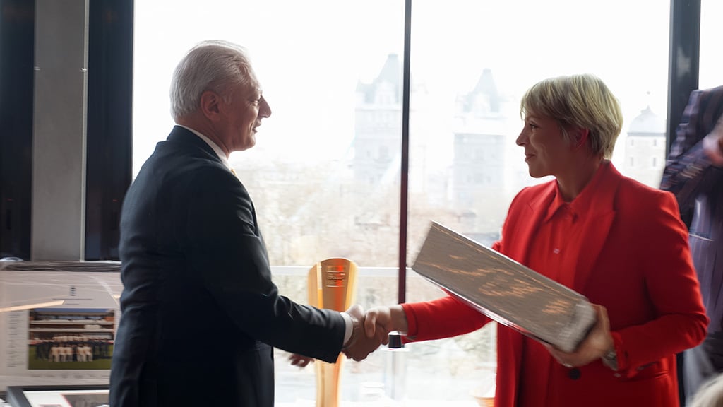 A woman in red presents a silver box to a man in a navy blue suit.