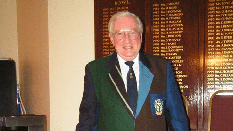 An elderly man wearing a blazer comprising many different fabrics and colours.