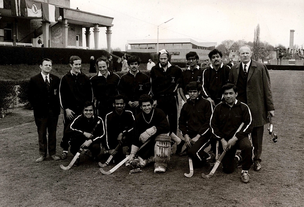 A team of male hockey players of various ethnicities, but mainly South Asian, wearing black and white tracksuits.