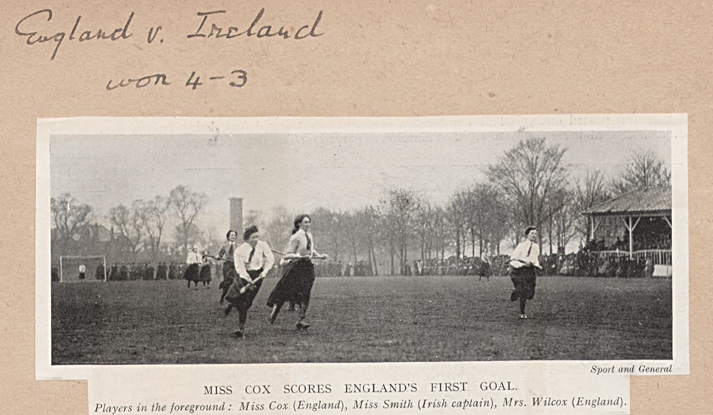 An action photograph from a women's hockey match with the players all wearing long, ankle-length skirts and blouses. The players are running towards the camera.