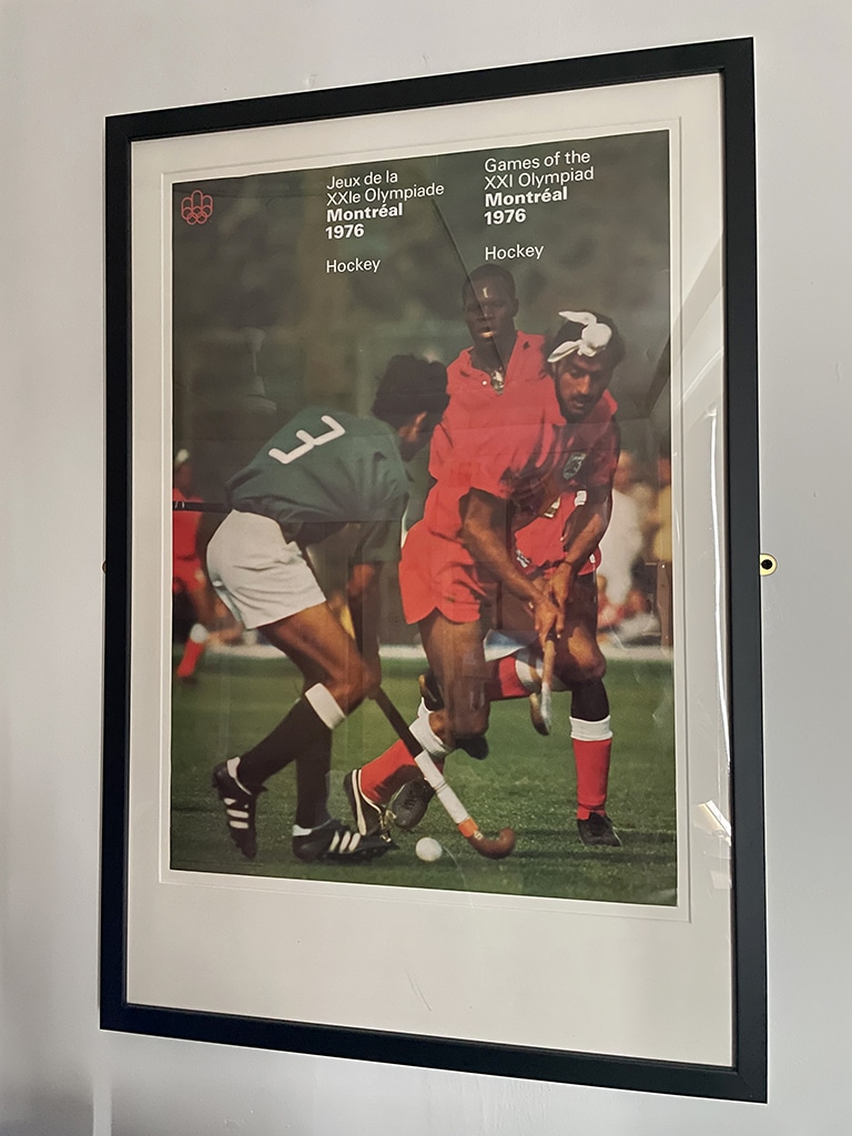 A poster mounted in a black frame hangs on a wall. Two Asian hockey players, one wearing red and the other green, compete for the ball.