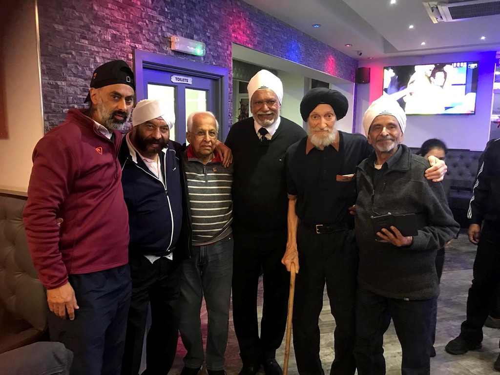 Six men of South Asian heritage stand with arms around one another in a room with disco lights.