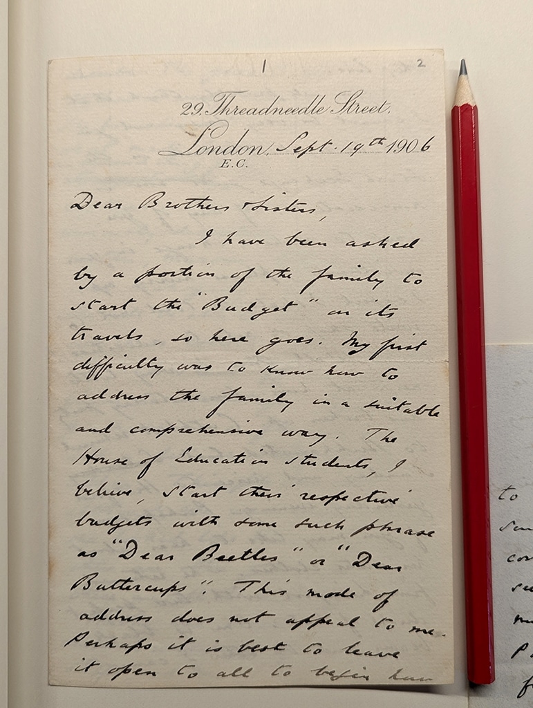 A piece of headed paper with filled with small, tight handwritten script sits adjacent to a red pencil.