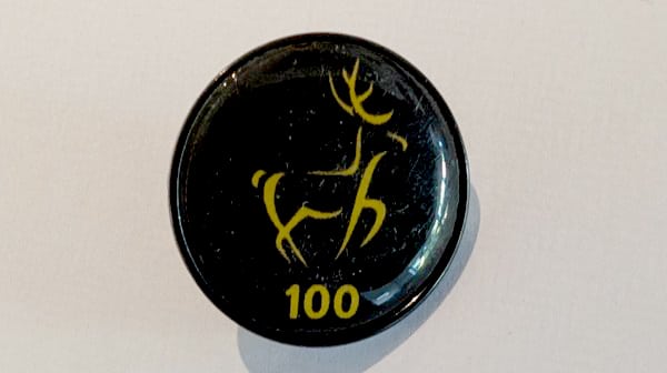A black circular badge with a yellow stag above the number 100