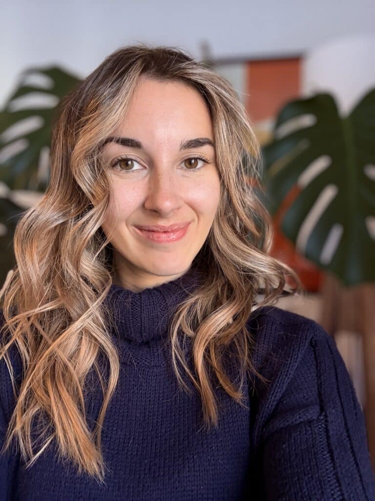 Profile photograph of a young woman with long, wavy brown hair and blonde highlights wearing a navy blue turtle-neck sweater.