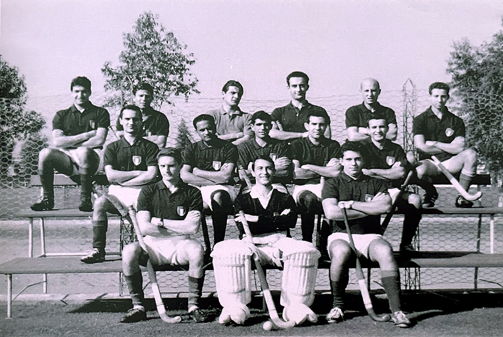 A team photograph of young, male hockey players wearing dark shirts are seated on tiered benches in three rows.