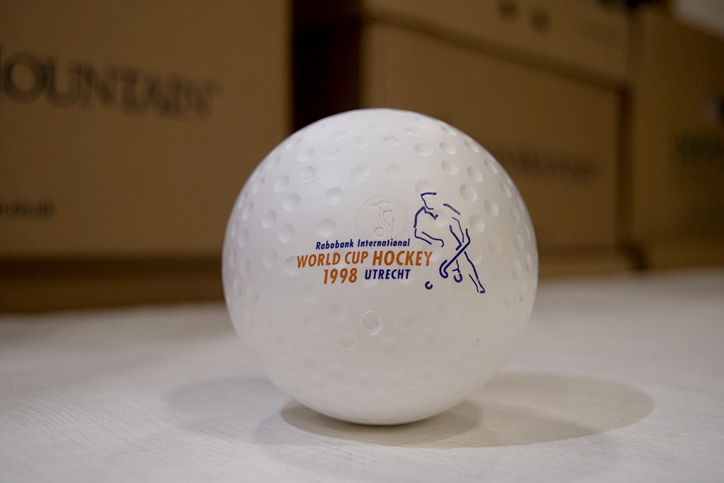 A white, dimpled plastic hockey ball with a figure of a hockey player outlined in blue.