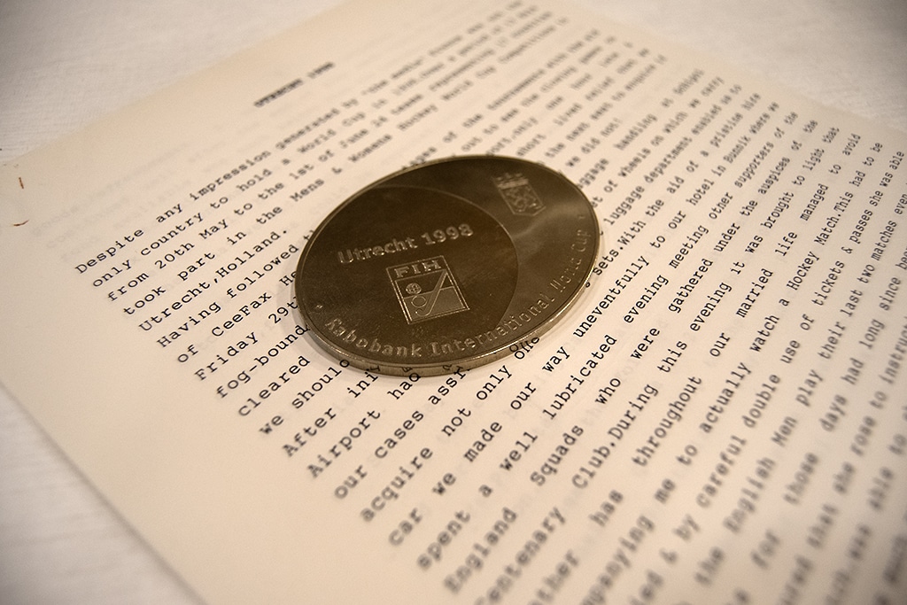 Circular metal commemorative medallion engraved with the International Hockey Federation emblem, resting on the pages of a typed report.
