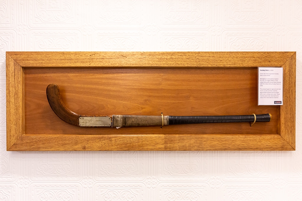 A wooden hockey stick with a twine grip mounted on a large wooden plaque.