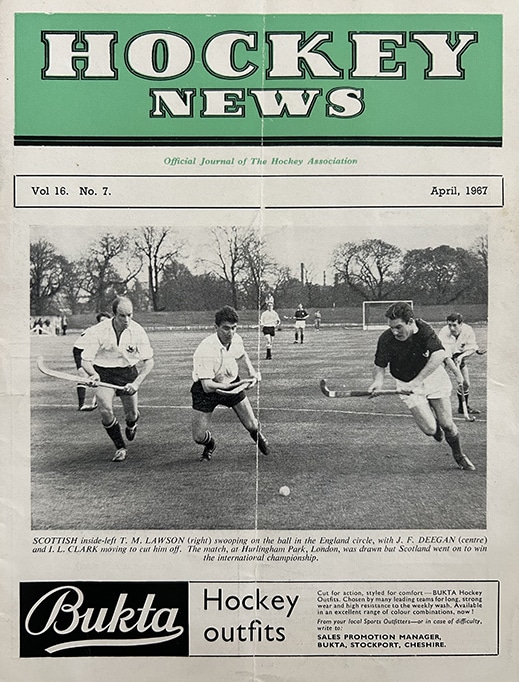 Cover page of a magazine featuring a black-and-white photograph of a hockey match with players running toward the ball. The cover includes publication details, a match caption, and a Bukta hockey equipment advertisement at the bottom.
